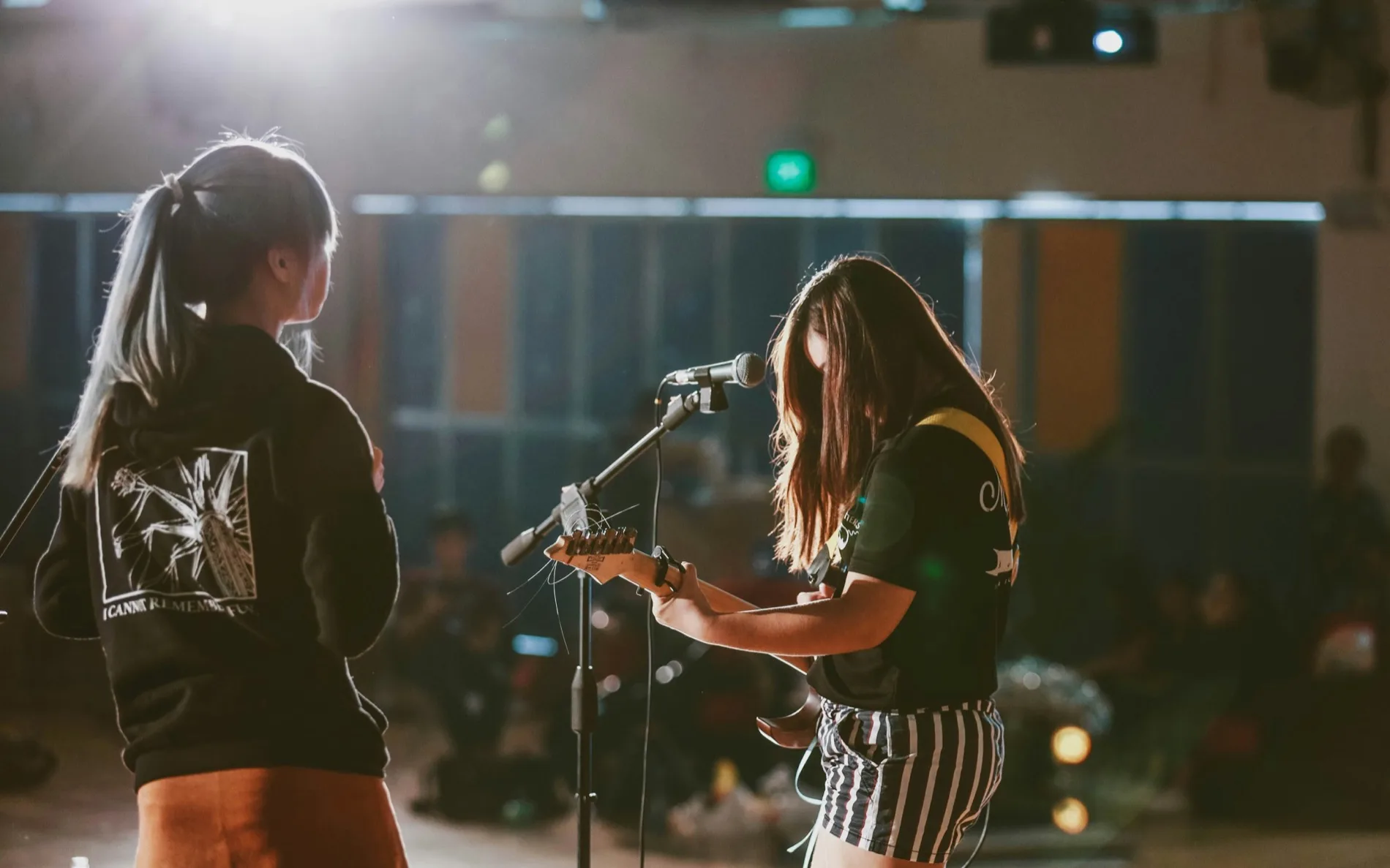 Two teenage musicians at a school holiday music camp in Perth, one playing electric guitar and singing into a microphone