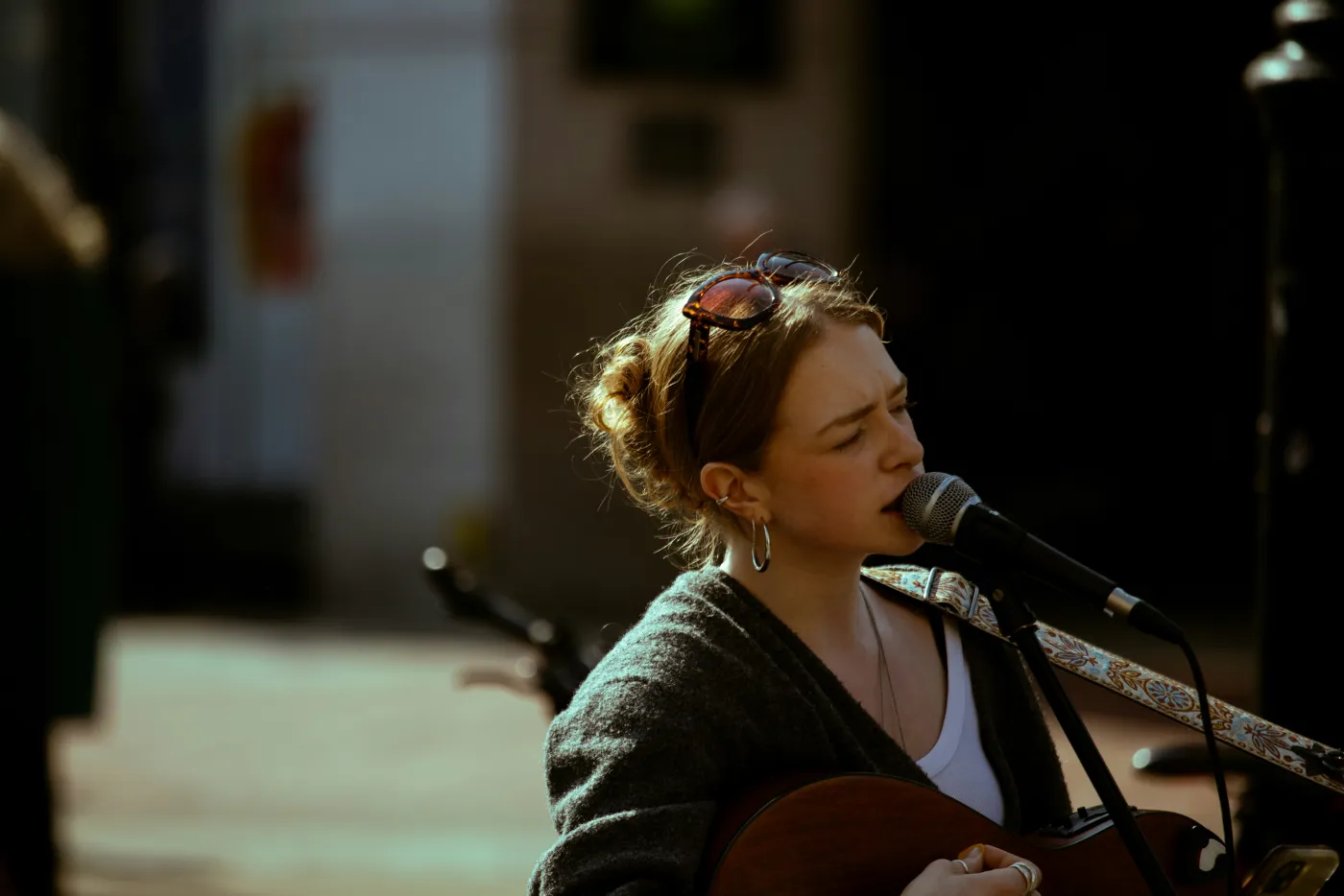 A young woman singing into a microphone while playing acoustic guitar