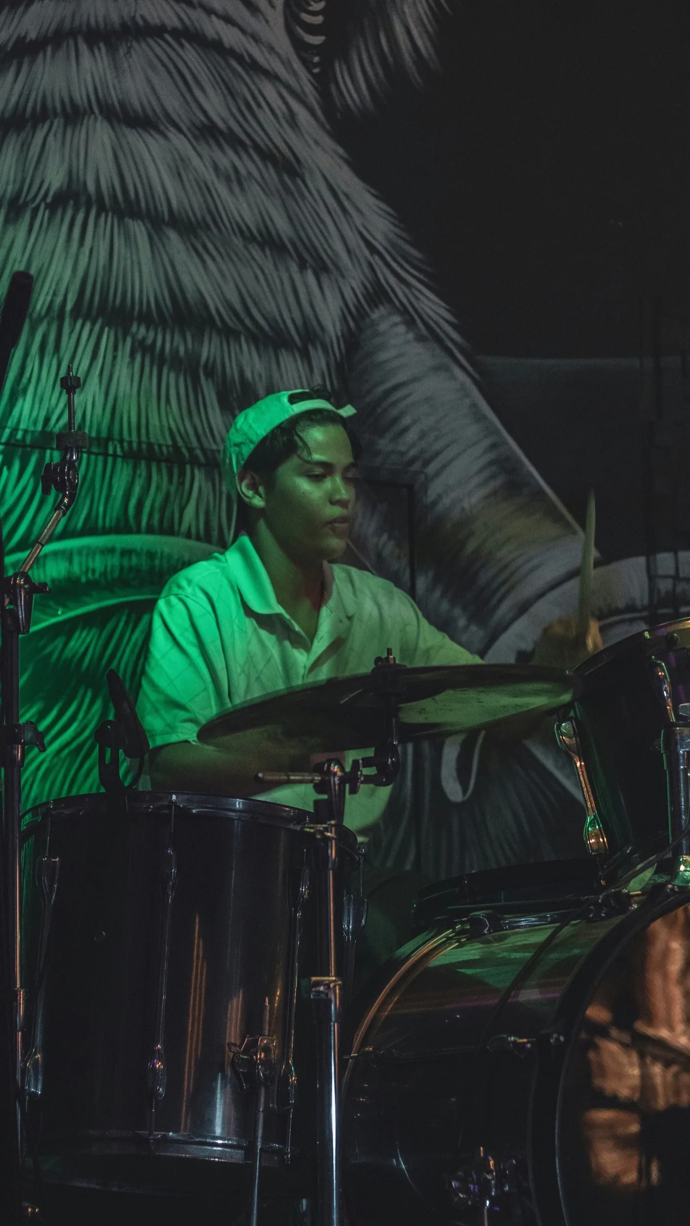 A young drummer performing under green stage light
