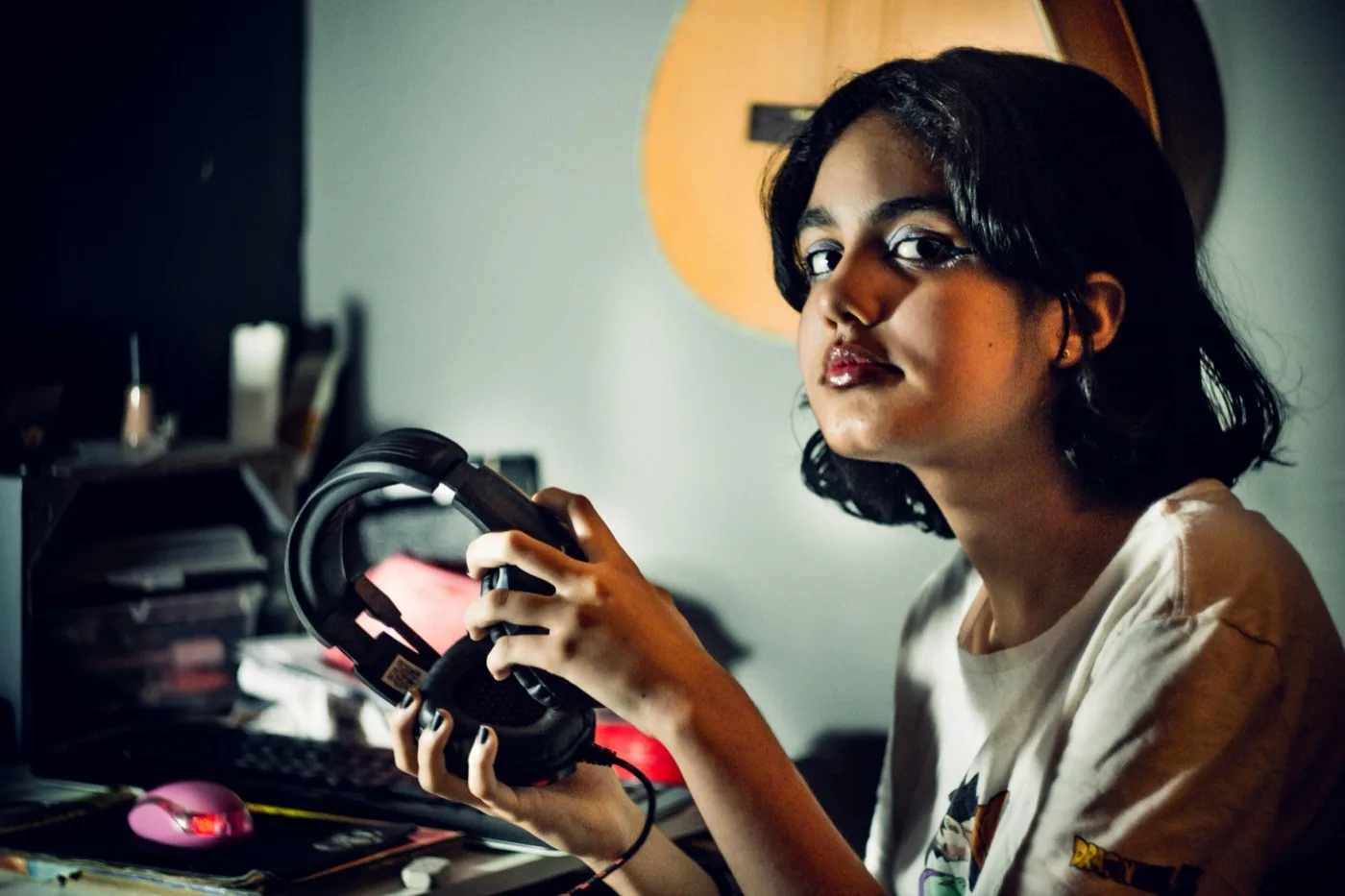 A teenage girl holding headphones next to an acoustic guitar